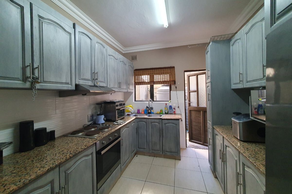 A functional kitchen featuring granite countertops, built-in oven, hob, extractor fan, and ample cabinetry, with direct access to an exterior area.