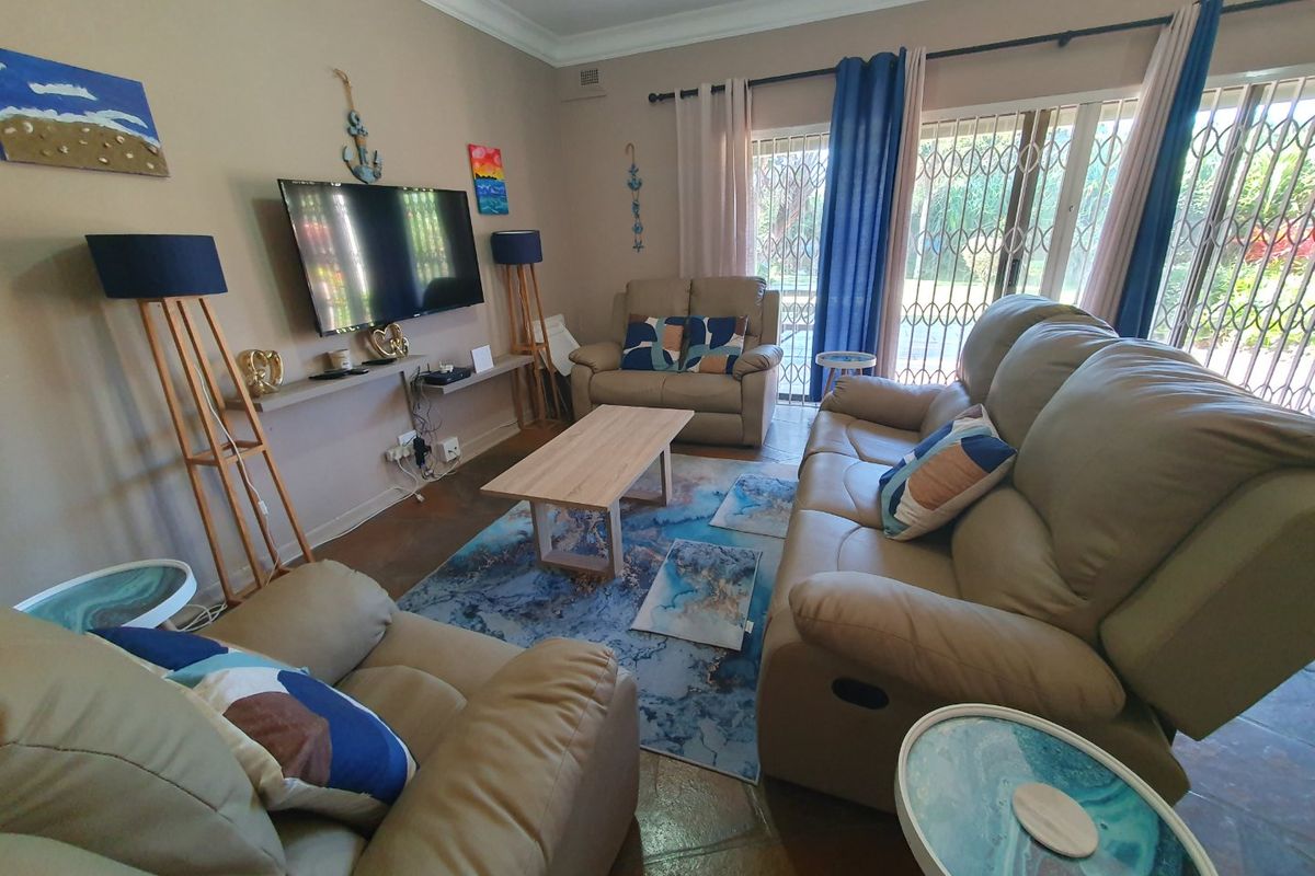 A comfortable living room featuring tiled flooring, crown molding, and large sliding glass doors with security gates leading to the outdoor area.