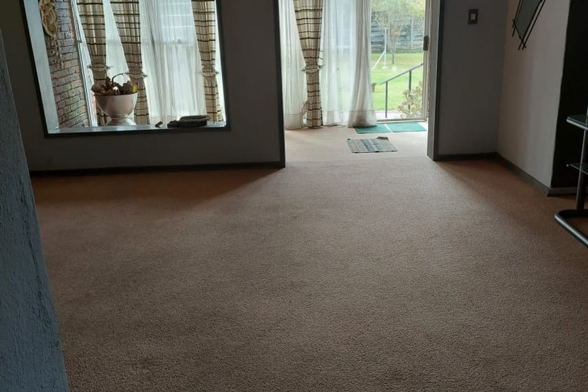 Spacious living area featuring fitted carpeting, exposed brick accents, and large sliding glass doors providing direct access to the rear garden.