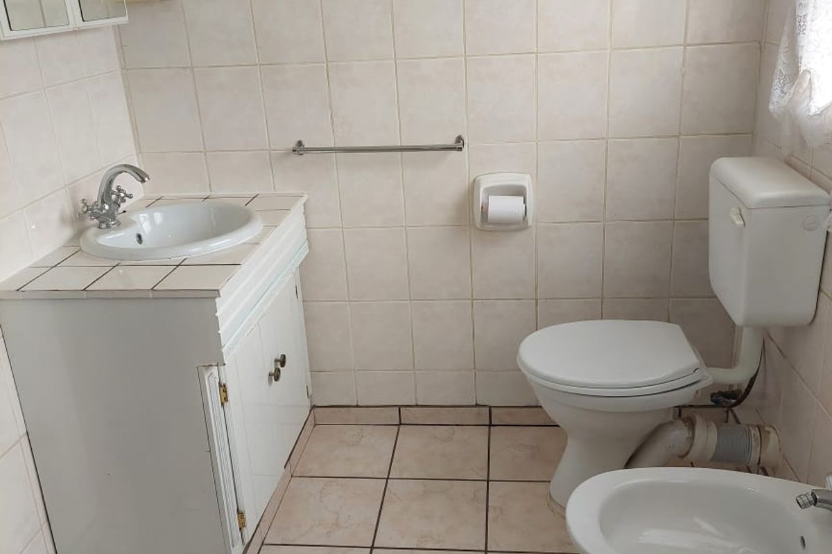 A functional bathroom featuring a vanity with basin, toilet, and bidet, finished with neutral wall and floor tiles.