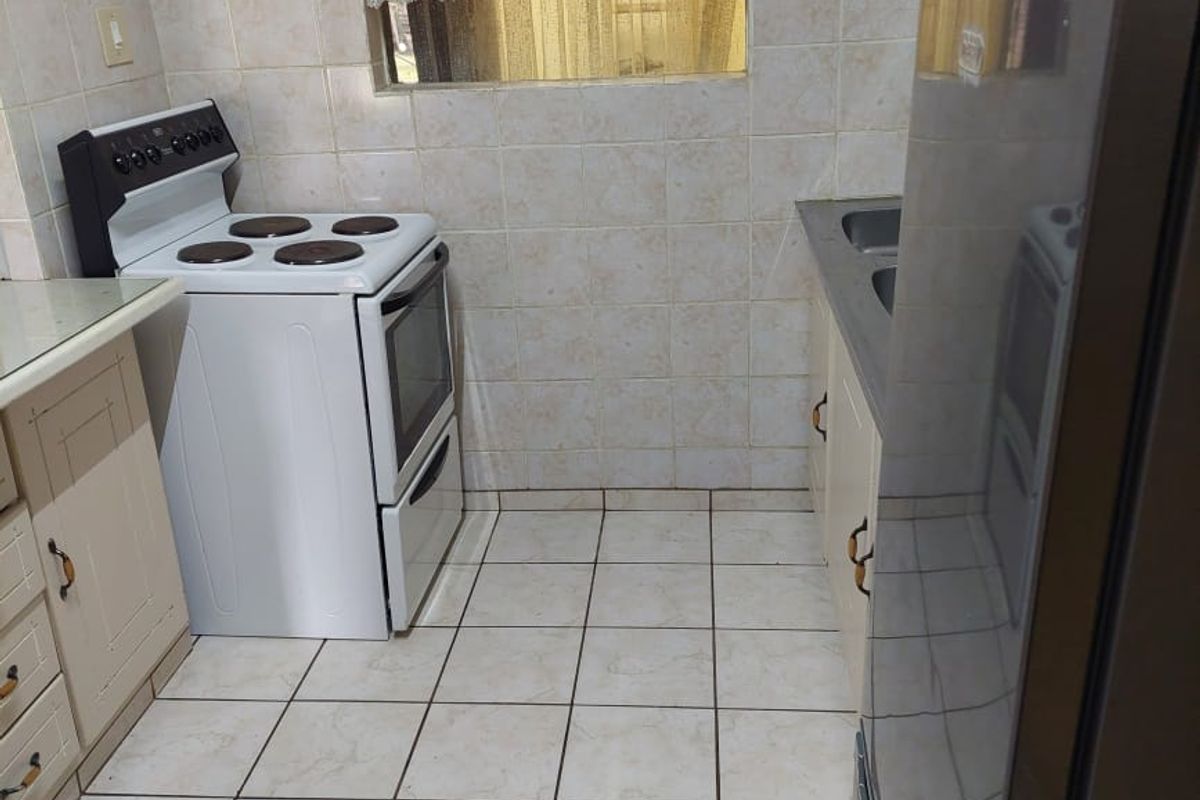A functional kitchen featuring tiled walls and flooring, built-in cabinetry, a stainless steel sink, and a freestanding stove.