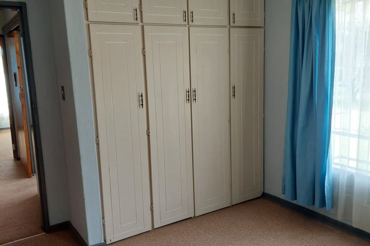 A clean, empty bedroom featuring neutral built-in cupboards, carpeted flooring, and a classic pendant light fixture, offering a blank canvas for personalization.