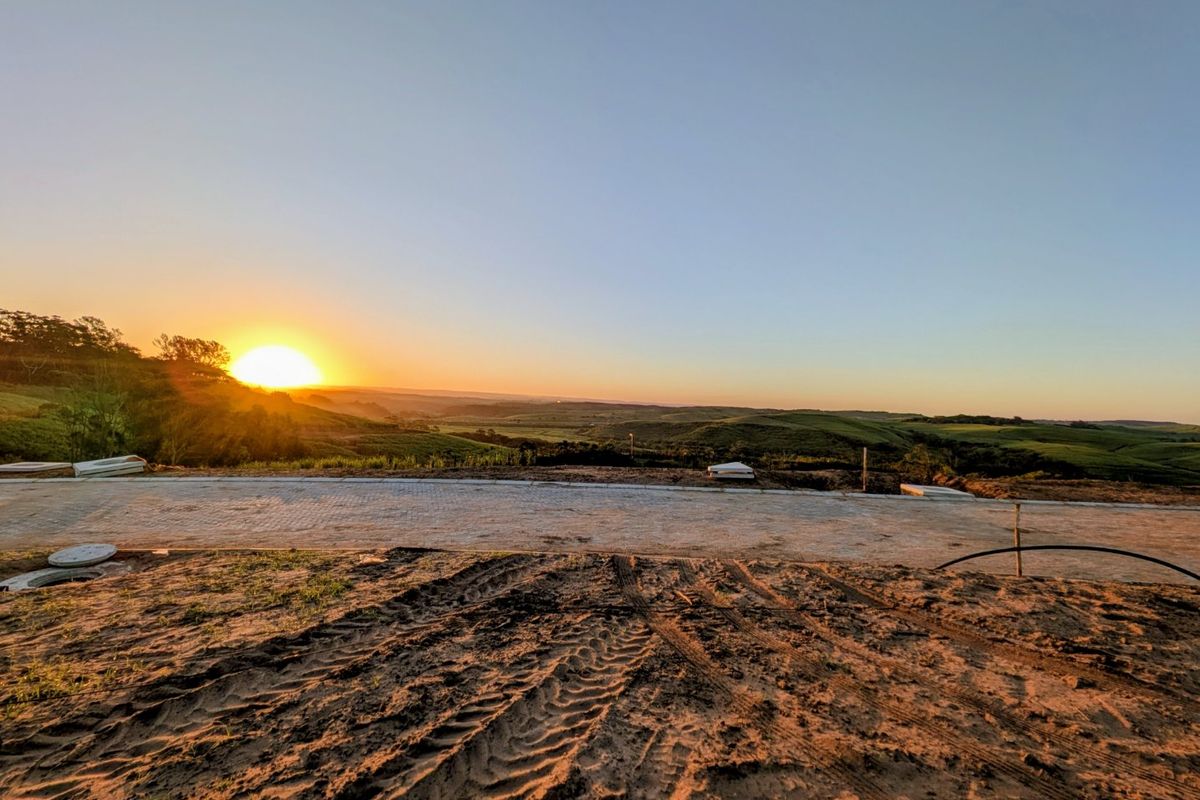 A scenic sunset view overlooking rolling hills and landscape from a vacant residential plot with an existing paved road.