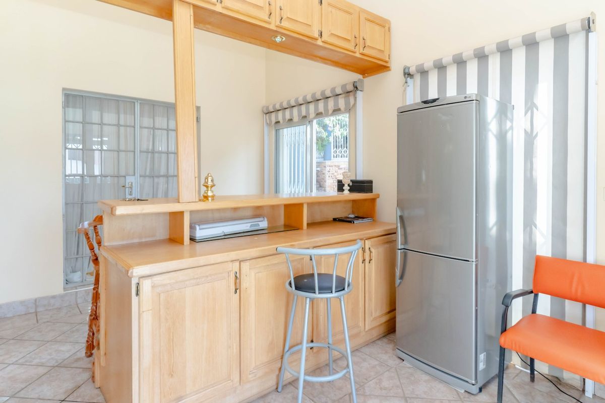 A functional kitchen area featuring built-in wooden cabinetry, a breakfast bar counter, and tiled flooring with access to an adjacent space.
