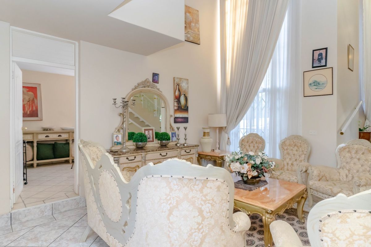 A spacious living room featuring double-height ceilings, large windows allowing ample natural light, and tiled flooring, creating an airy and open atmosphere.