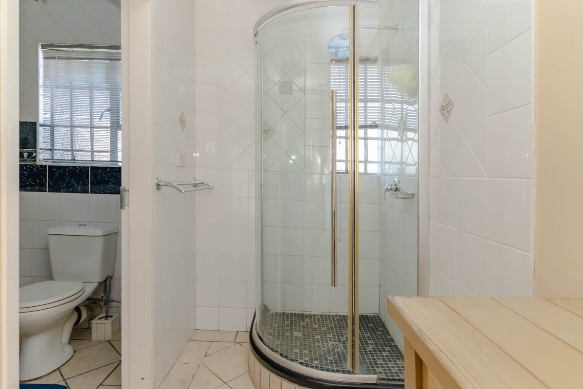 A functional bathroom featuring a curved glass shower enclosure, ceramic wall and floor tiling, and a standard toilet.