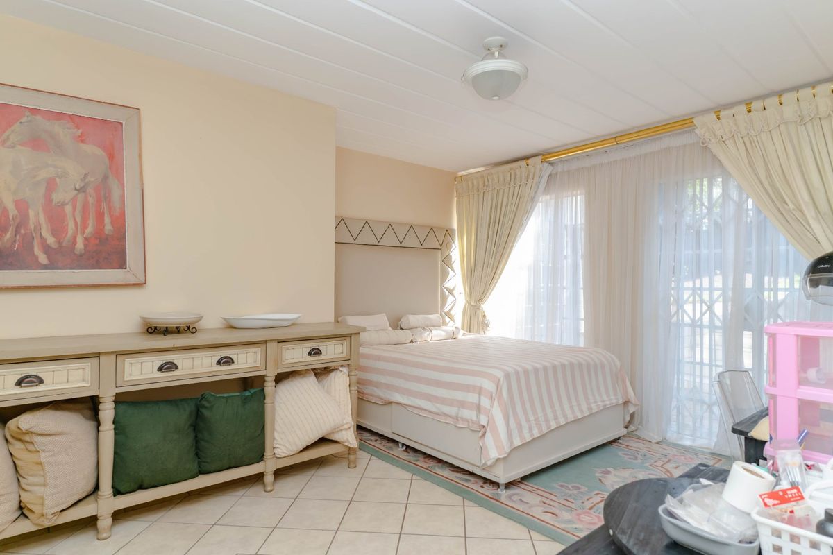 A bedroom featuring tiled flooring, a ceiling light fixture, and a sliding glass door with an integrated security gate providing access to the exterior.