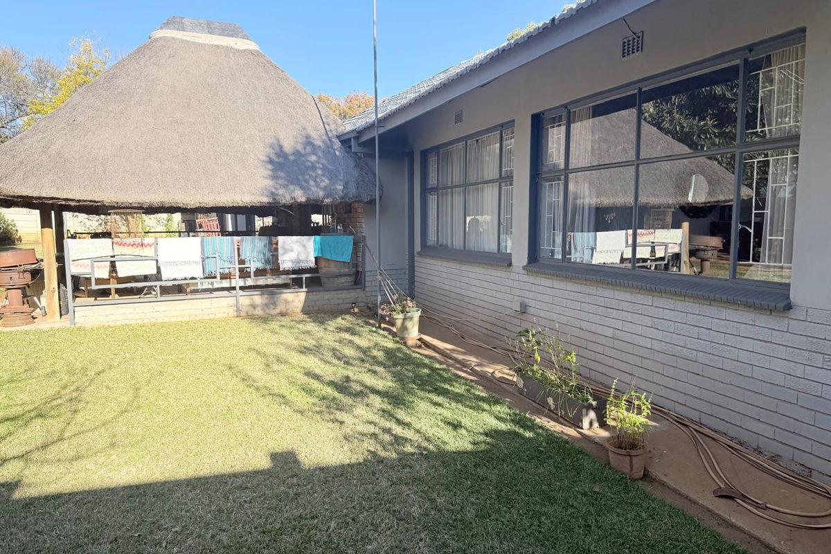Rear view of the property featuring a lawn, a thatched lapa entertainment area, and large steel-framed windows along the main building facade.