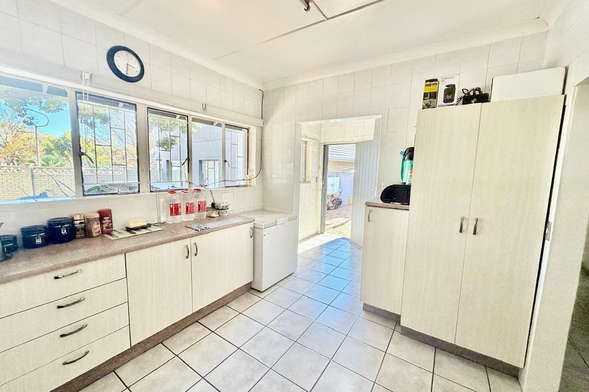 A functional kitchen featuring tiled walls and flooring, ample built-in cabinetry, and large windows providing natural light, with direct access to the rear exterior.