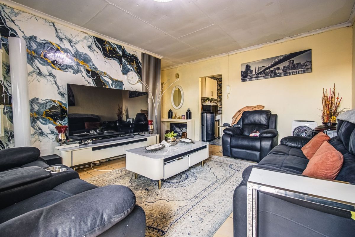 Living room featuring tiled flooring, a decorative marble-effect feature wall, and a built-in fireplace, offering a distinct layout with access to the kitchen area.