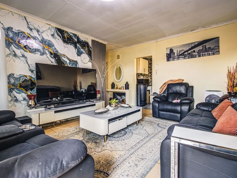 Living room featuring tiled flooring, a decorative marble-effect feature wall, and a built-in fireplace, offering a distinct layout with access to the kitchen area.