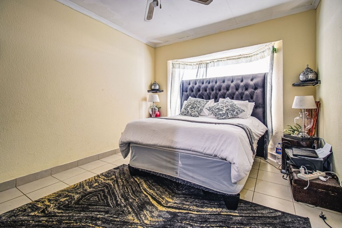 A bedroom featuring tiled flooring, a ceiling fan, and a bay window. The ceiling shows visible signs of water damage and staining.
