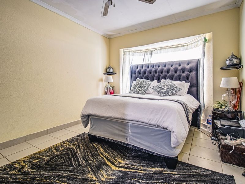 A bedroom featuring tiled flooring, a ceiling fan, and a bay window. The ceiling shows visible signs of water damage and staining.
