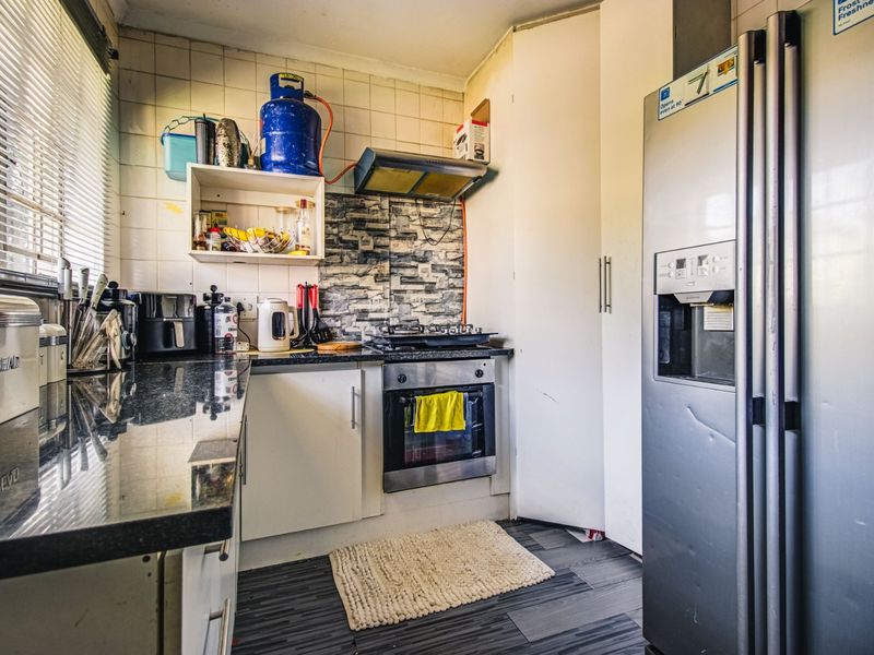 Compact kitchen featuring granite countertops, built-in oven, gas hob, and extractor fan, with tiled backsplash and ample storage cabinetry.