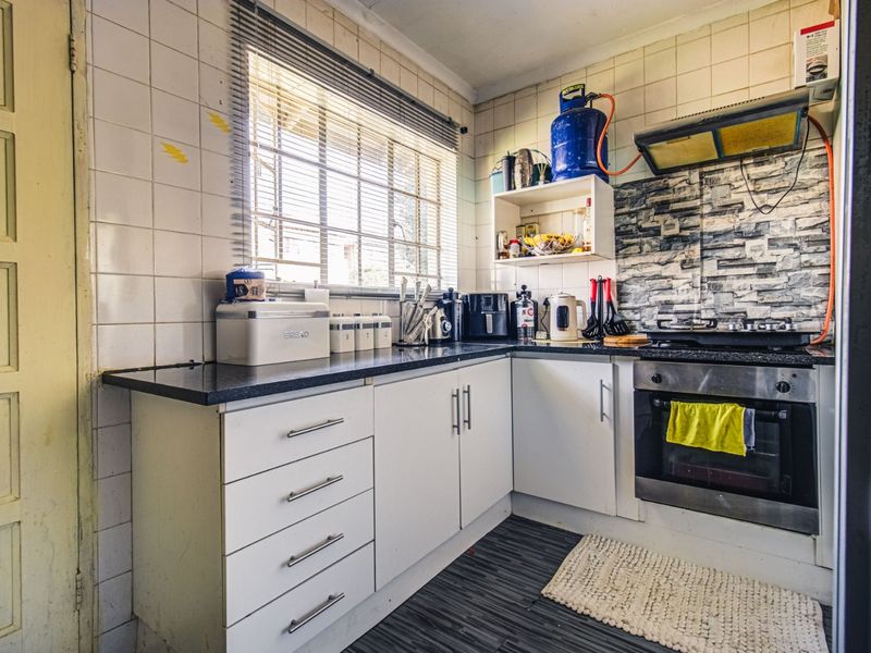 A compact kitchen featuring white cabinetry, granite countertops, a built-in oven with gas hob, and tiled splashbacks, requiring some cosmetic updates.