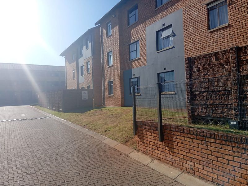 Exterior view of a multi-story apartment complex featuring face brick facade, paved driveway, and secure perimeter fencing.