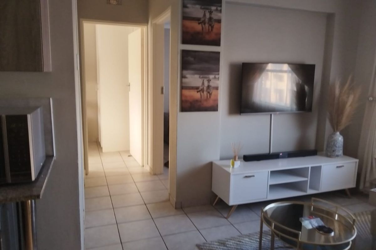 A living room area featuring tiled flooring and a wall-mounted television, with access to internal hallways.