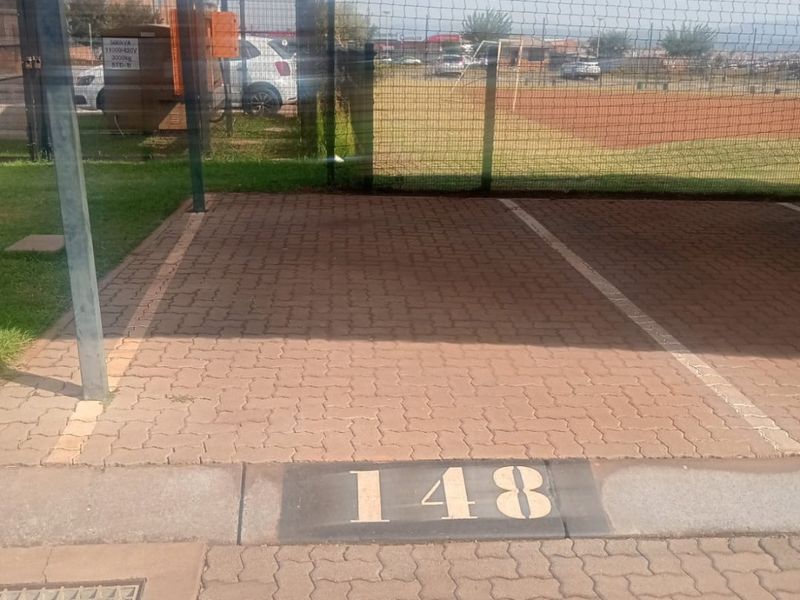 A designated covered parking bay numbered 148, featuring paved surfacing and a metal carport structure within a secure complex.