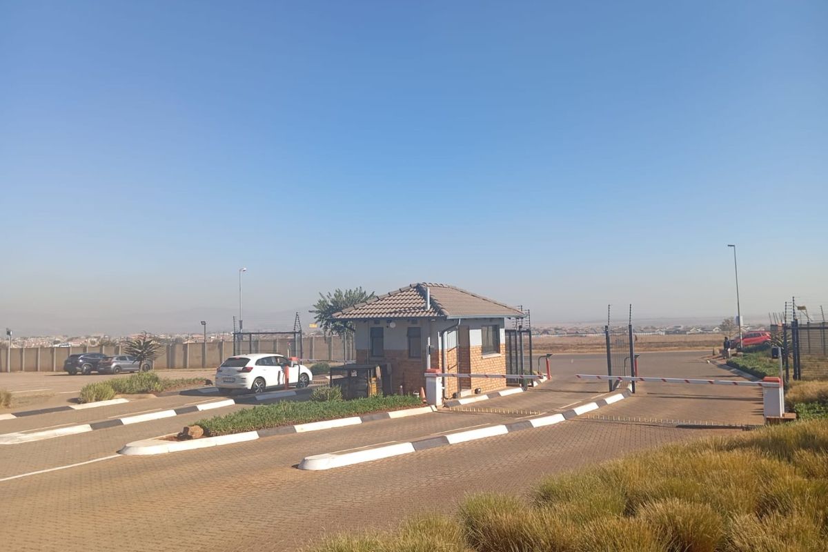 The entrance to the apartment complex features a secure guard house, automated boom gates, and a well-maintained paved driveway.