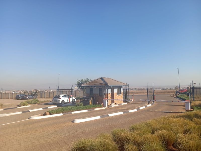 The entrance to the apartment complex features a secure guard house, automated boom gates, and a well-maintained paved driveway.