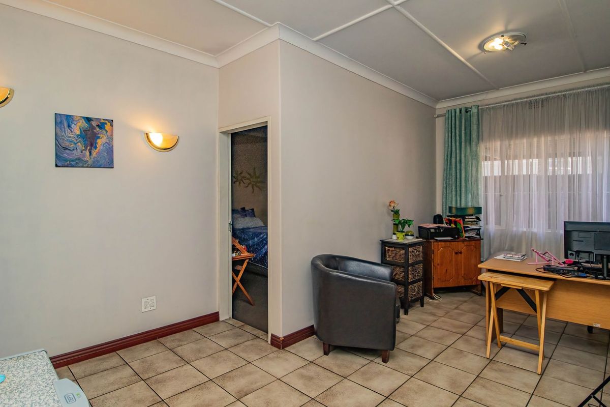 A living area featuring tiled flooring, coved ceilings, and wall-mounted sconce lighting, providing a functional space with access to an adjacent bedroom.