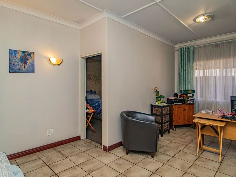 A living area featuring tiled flooring, coved ceilings, and wall-mounted sconce lighting, providing a functional space with access to an adjacent bedroom.