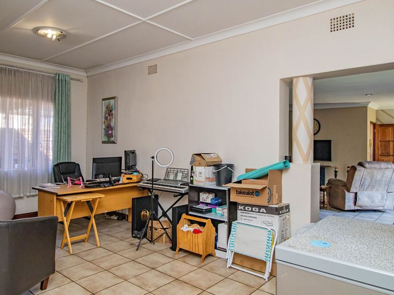 A multi-purpose living area featuring tiled flooring and decorative ceiling panels, with an open-plan layout connecting to an adjacent room.