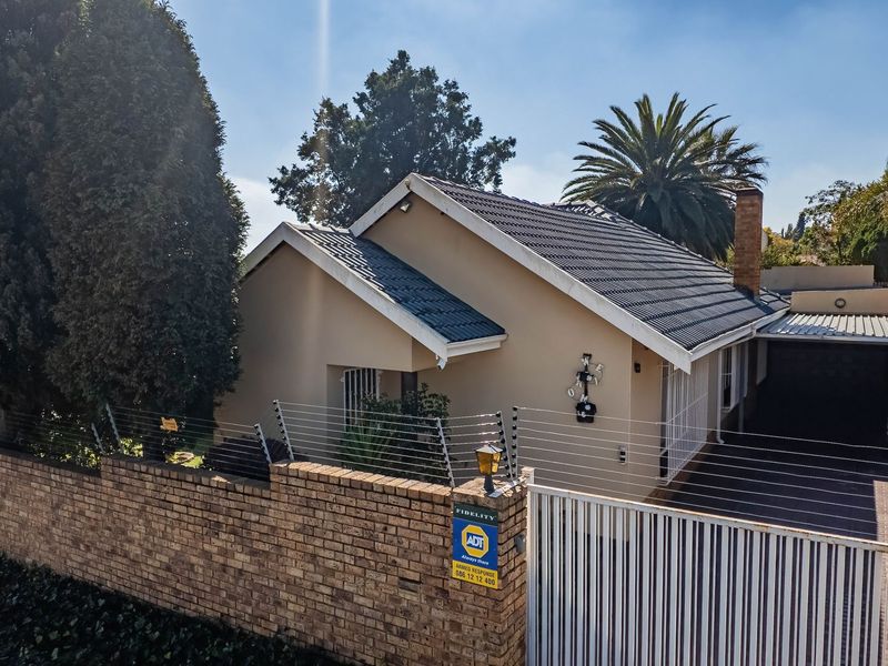 Front view of a residential property featuring a tiled roof, brick boundary wall with electric fencing, and a secure sliding gate entrance.