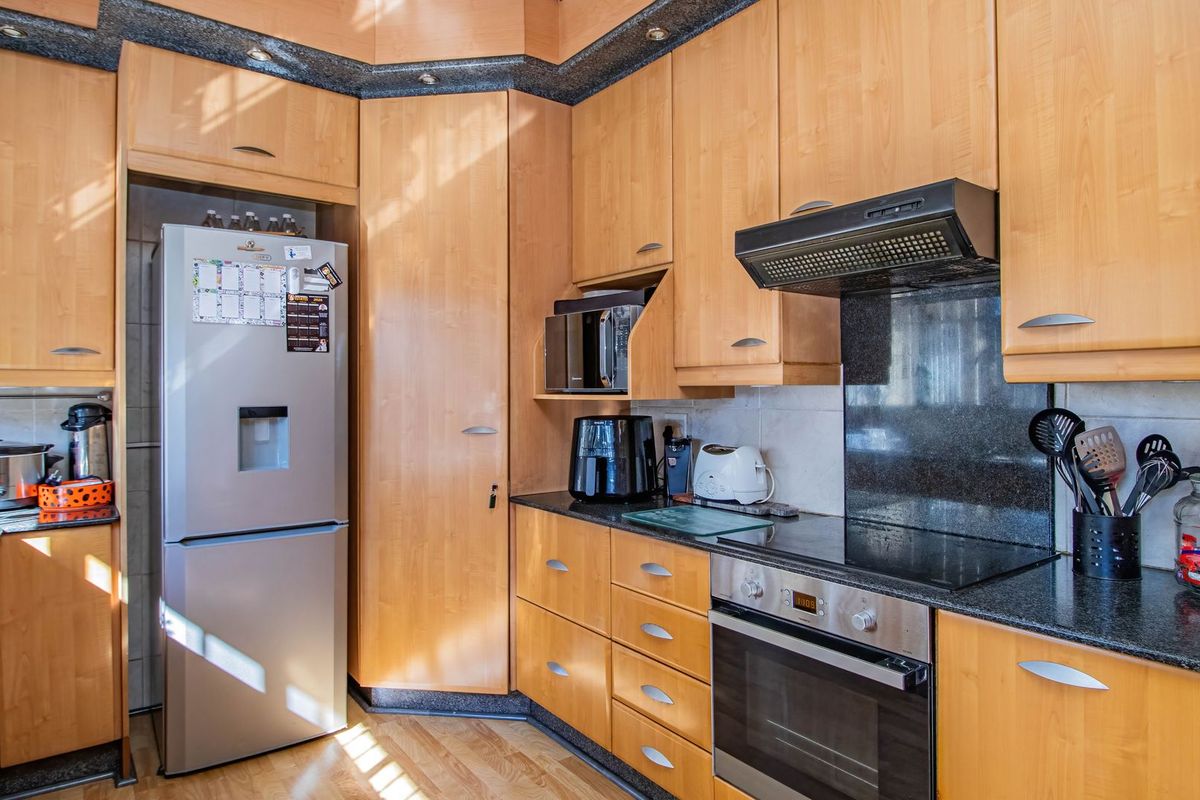 A functional kitchen featuring light wood cabinetry, granite countertops, and integrated appliances including an oven, hob, and extractor fan.