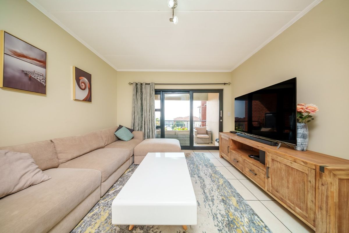 A well-maintained living room featuring tiled flooring, coved ceilings, and a sliding glass door providing access to an outdoor balcony area.