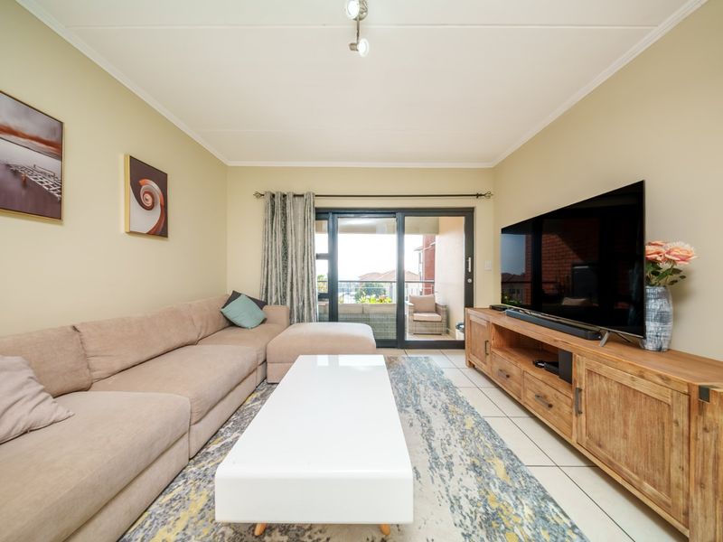 A well-maintained living room featuring tiled flooring, coved ceilings, and a sliding glass door providing access to an outdoor balcony area.