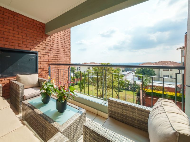 A covered balcony featuring a built-in braai, tiled flooring, and a metal balustrade, offering pleasant views of the surrounding residential area.