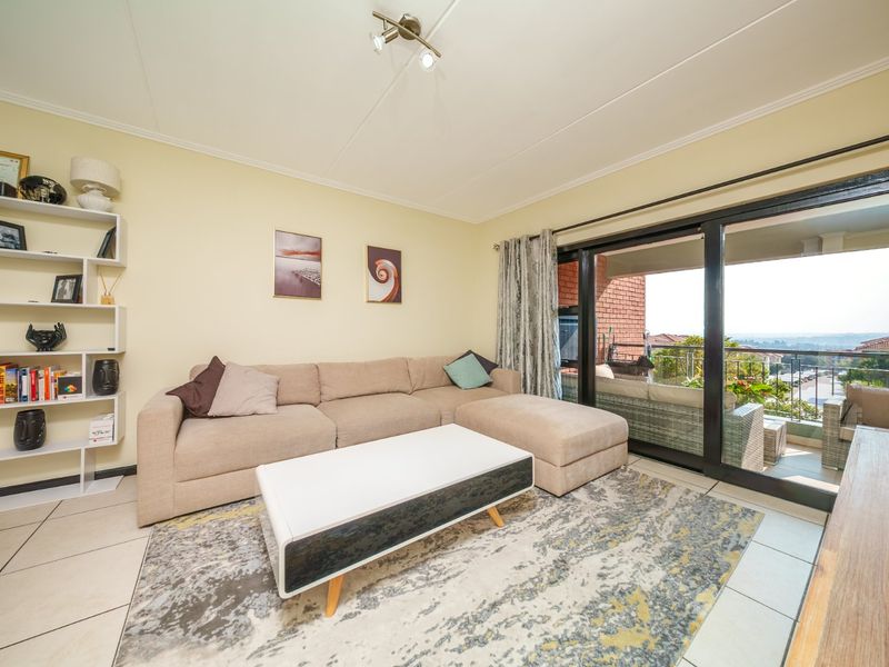 A comfortable living room featuring tiled flooring, a built-in shelving unit, and large sliding glass doors that open onto a balcony with scenic views.