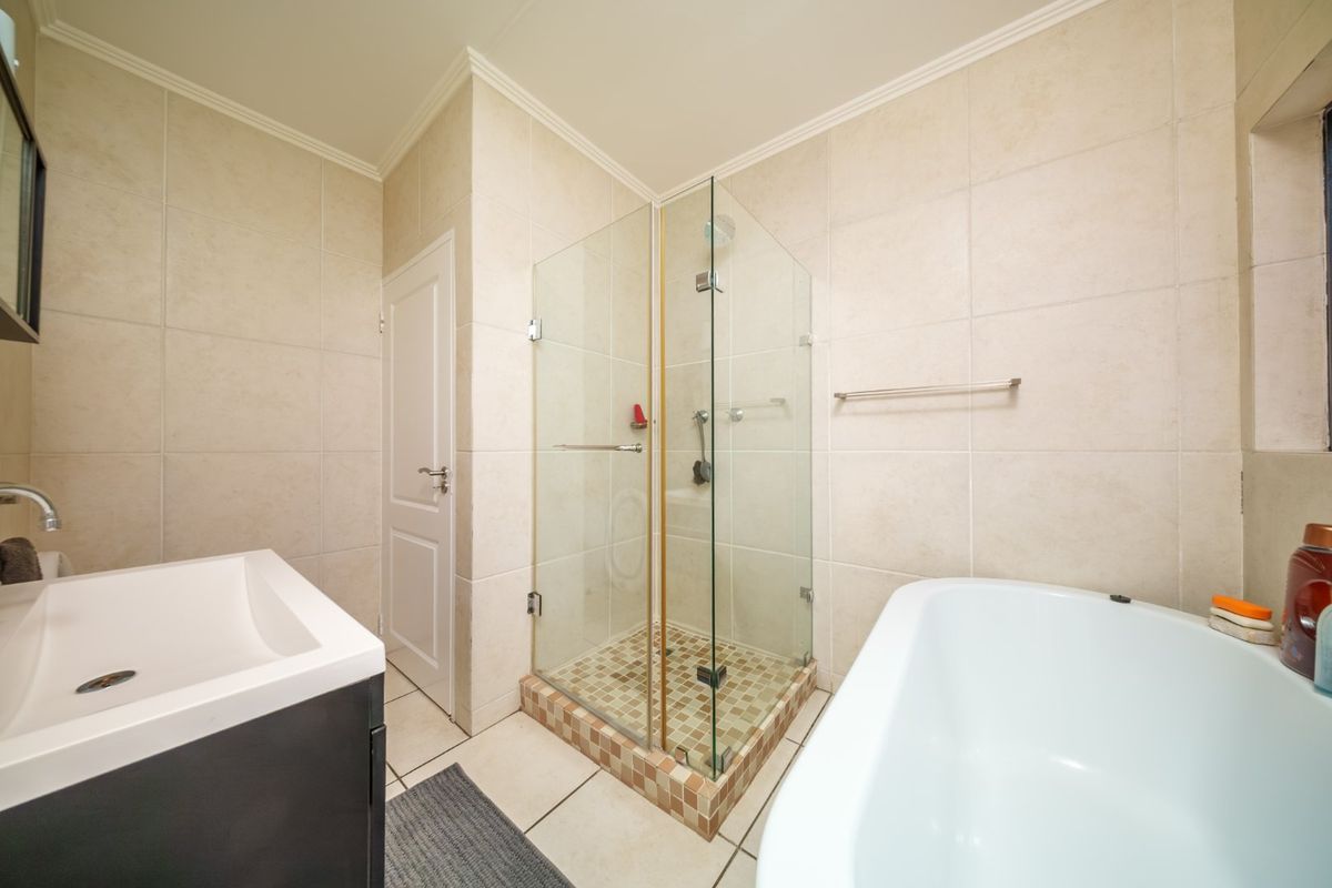 A well-maintained bathroom featuring a glass-enclosed shower, a modern freestanding bathtub, and neutral ceramic tiling throughout.