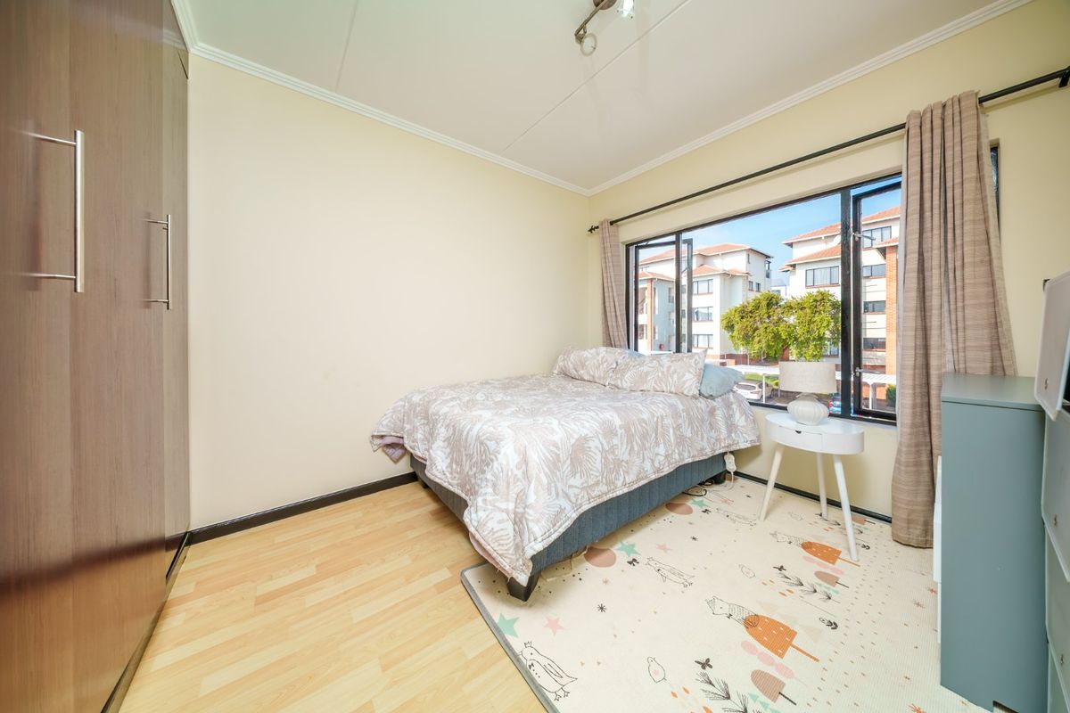 A functional bedroom featuring laminate flooring, a built-in wardrobe, and a large window providing natural light and views of the surrounding apartment complex.