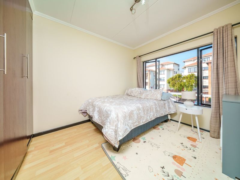 A functional bedroom featuring laminate flooring, a built-in wardrobe, and a large window providing natural light and views of the surrounding apartment complex.