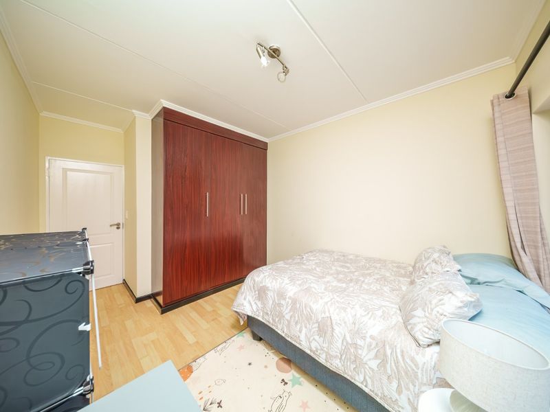 A bedroom featuring laminate flooring, a built-in wooden wardrobe, and neutral wall finishes, providing a functional and well-lit living space.