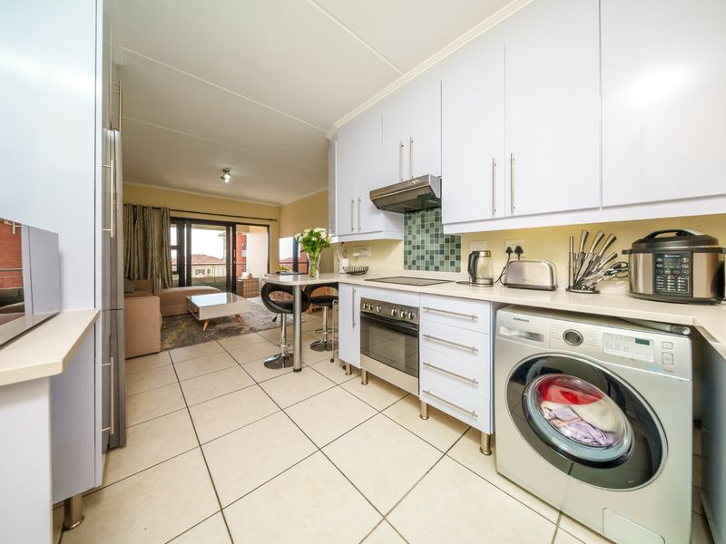 Open-plan kitchen and living area featuring light-toned cabinetry, tiled flooring, and a mosaic splashback, flowing seamlessly into the adjacent lounge space.
