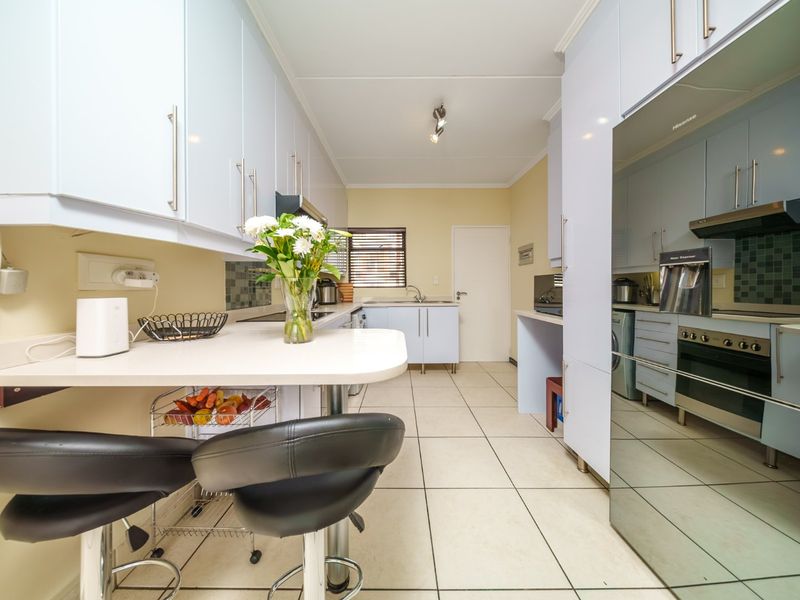 A functional galley-style kitchen featuring light blue cabinetry, tiled flooring, a built-in oven with extractor fan, and a breakfast bar area.