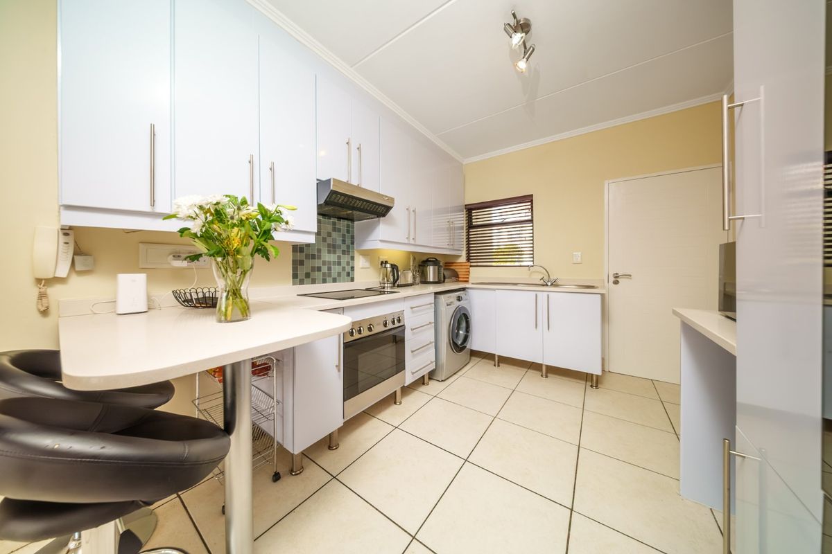 A functional kitchen featuring white cabinetry, a built-in oven and hob, tiled backsplash, and a convenient breakfast counter with tiled flooring throughout.