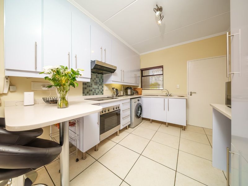 A functional kitchen featuring white cabinetry, a built-in oven and hob, tiled backsplash, and a convenient breakfast counter with tiled flooring throughout.
