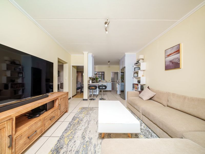 Open-plan living area featuring tiled floors and a connected kitchen with breakfast bar, offering a functional and versatile layout for modern apartment living.