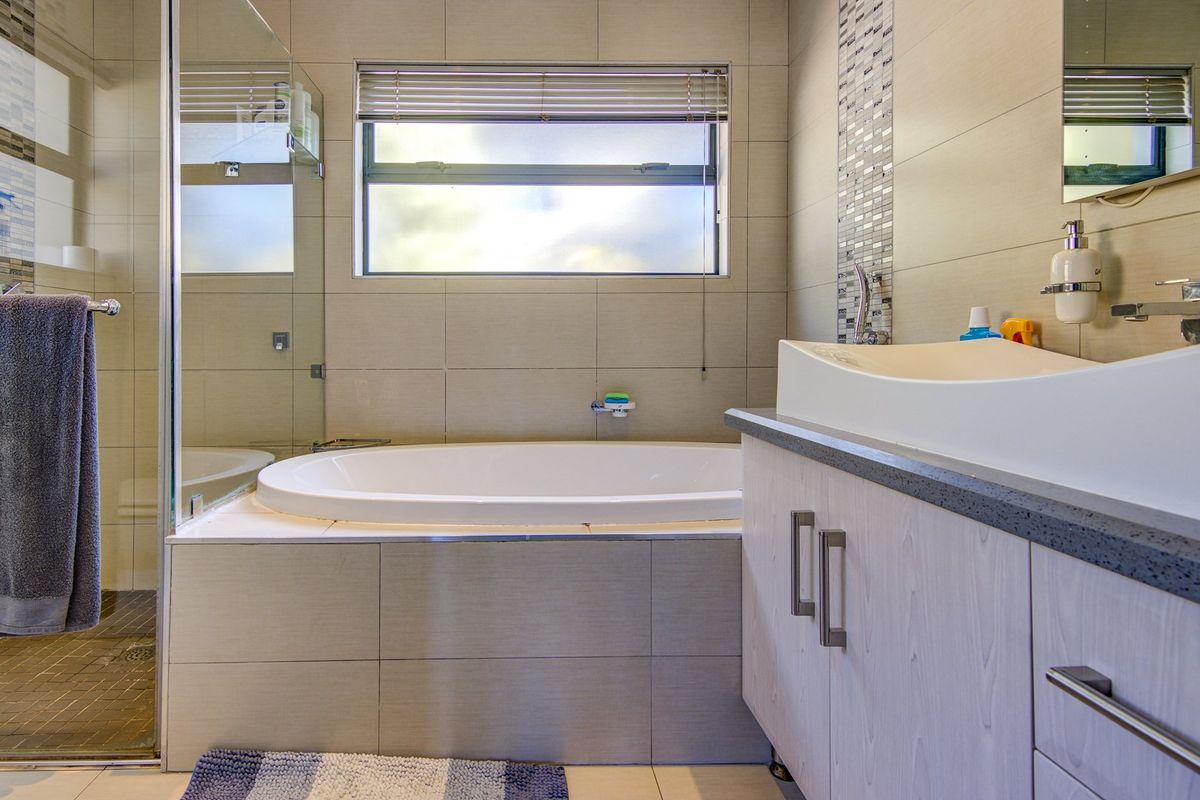 Modern bathroom featuring a built-in bathtub, glass-enclosed shower, vanity cabinet with a vessel sink, and neutral wall tiling.
