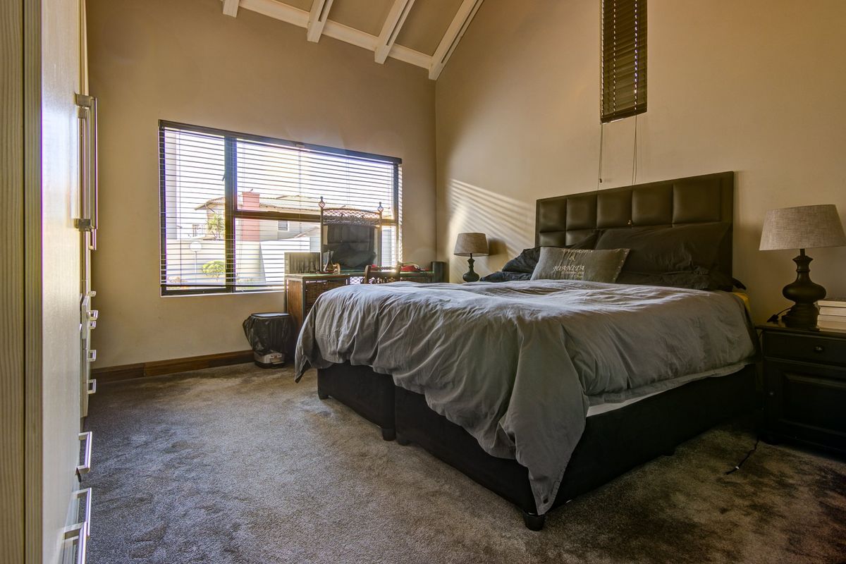 Spacious bedroom featuring a high vaulted ceiling with exposed rafters, carpeted flooring, and built-in storage cupboards.