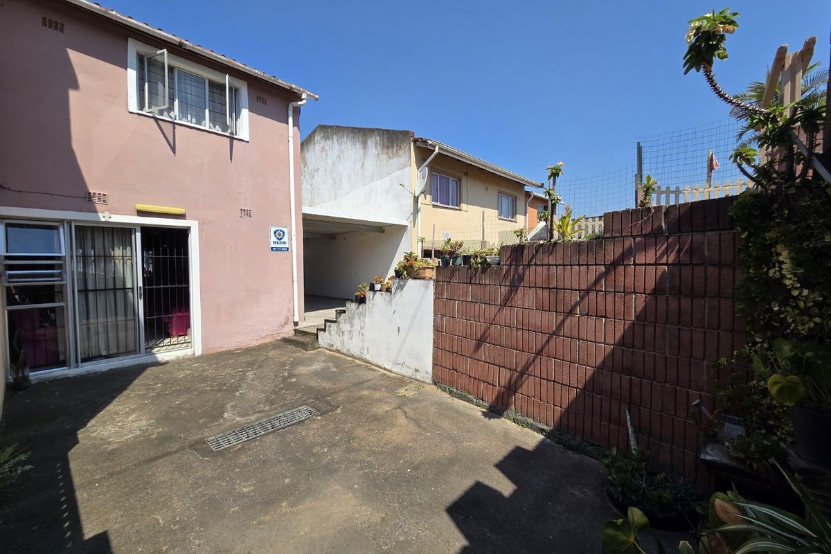Rear exterior view of the property featuring a paved courtyard area, brick boundary wall, and access via a sliding glass door.