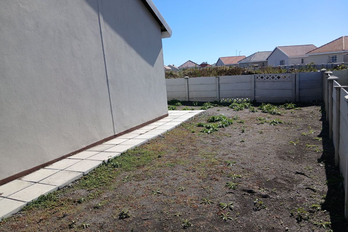 A side yard area featuring a paved walkway along the exterior wall and a large, unlandscaped garden space enclosed by precast concrete boundary walls.