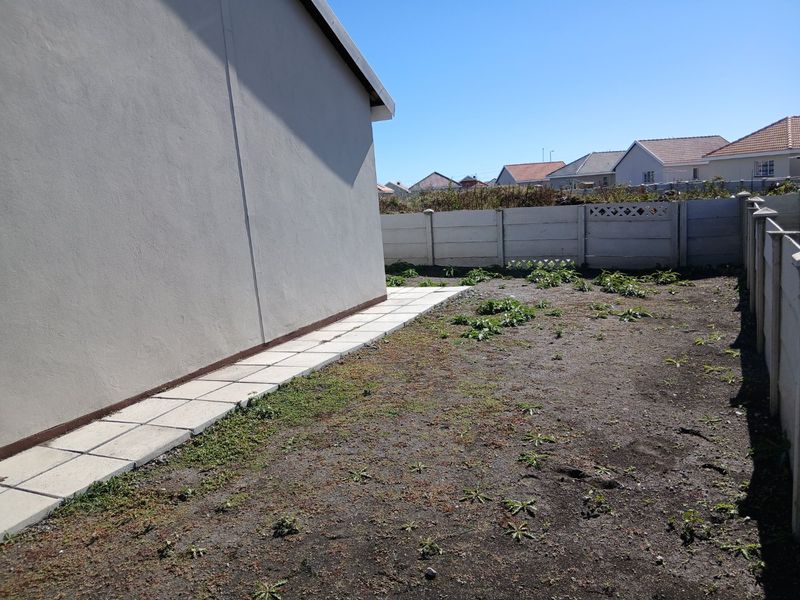 A side yard area featuring a paved walkway along the exterior wall and a large, unlandscaped garden space enclosed by precast concrete boundary walls.