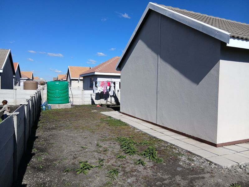 Rear exterior view of the property featuring a paved walkway, precast concrete boundary wall, and a water storage tank in the garden area.