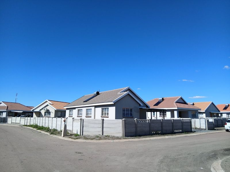 Street view of a residential neighbourhood featuring detached houses with tiled roofs, solar water heating systems, and precast concrete boundary walls.