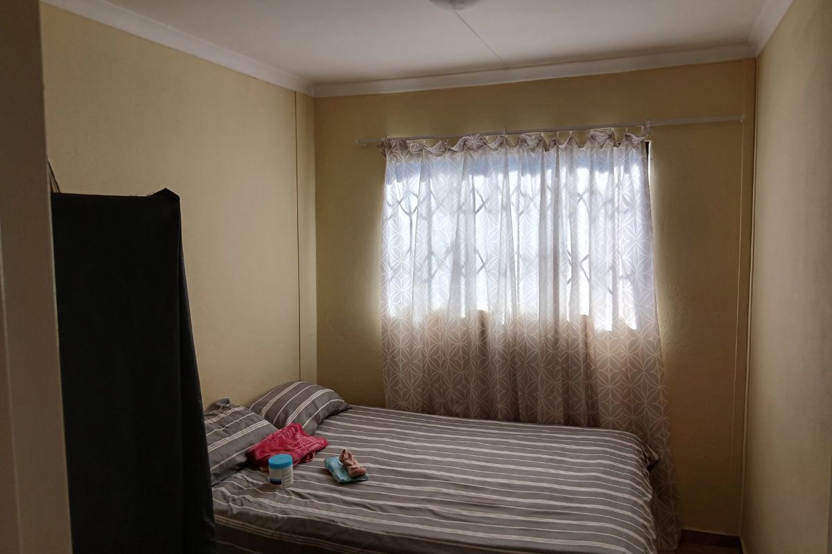 A functional bedroom featuring a window with a security gate and neutral wall finishes.